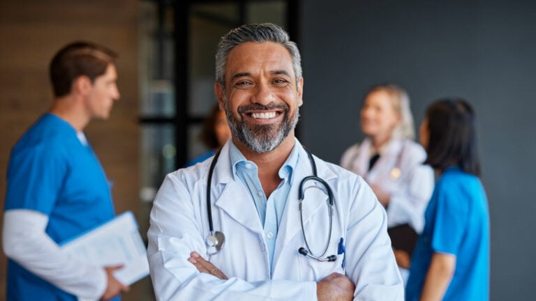 Experienced doctor smiling healthcare professional in hospital setting with medical team.