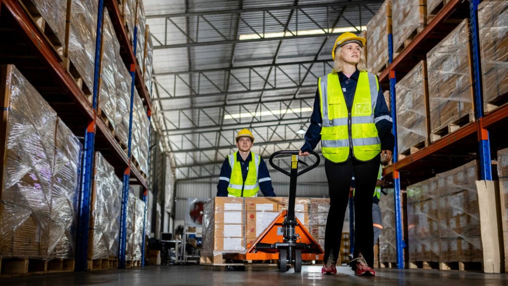 Efficient warehouse workers in safety vests managing logistics with pallet jacks at Concentrus.