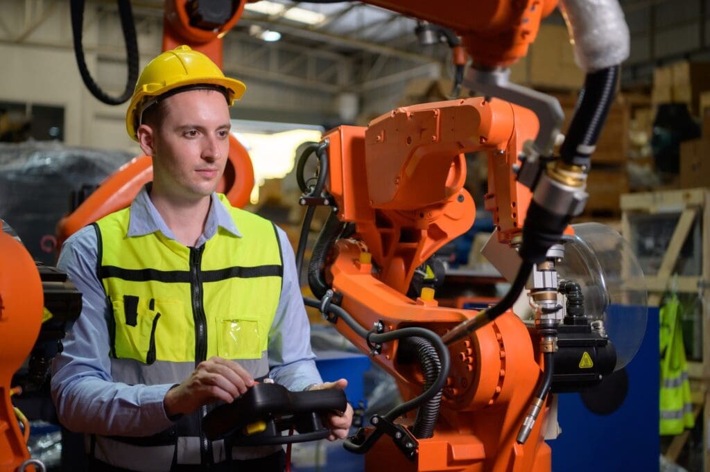 Robotic industrial automation in manufacturing with a technician operating a robotic arm.
