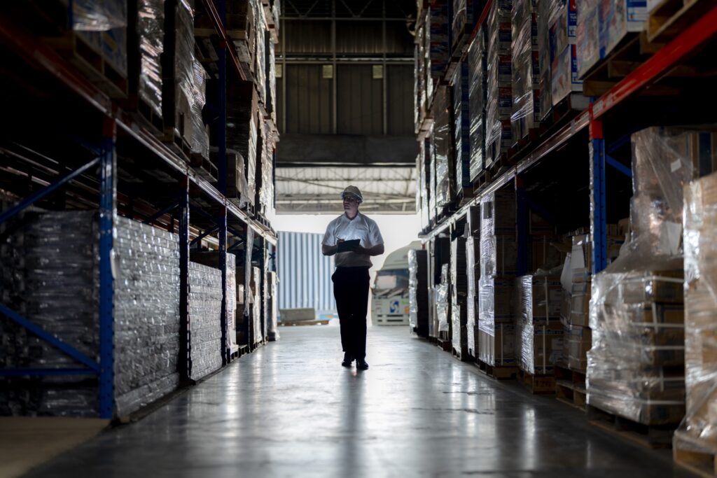 Inventory warehouse worker inspecting pallets of products in a large storage facility.