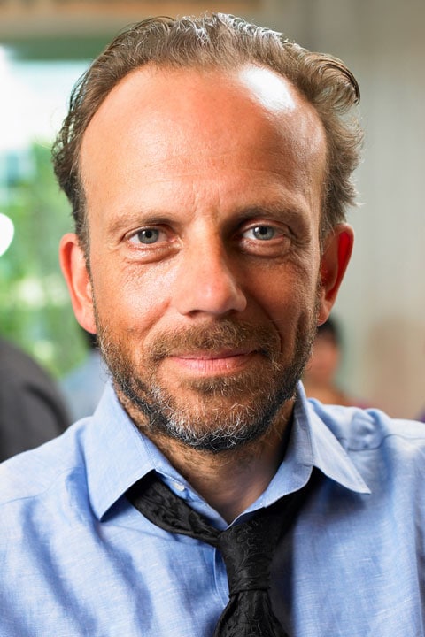 Caucasian man with a beard wearing a blue shirt and loosened black tie at a corporate event.