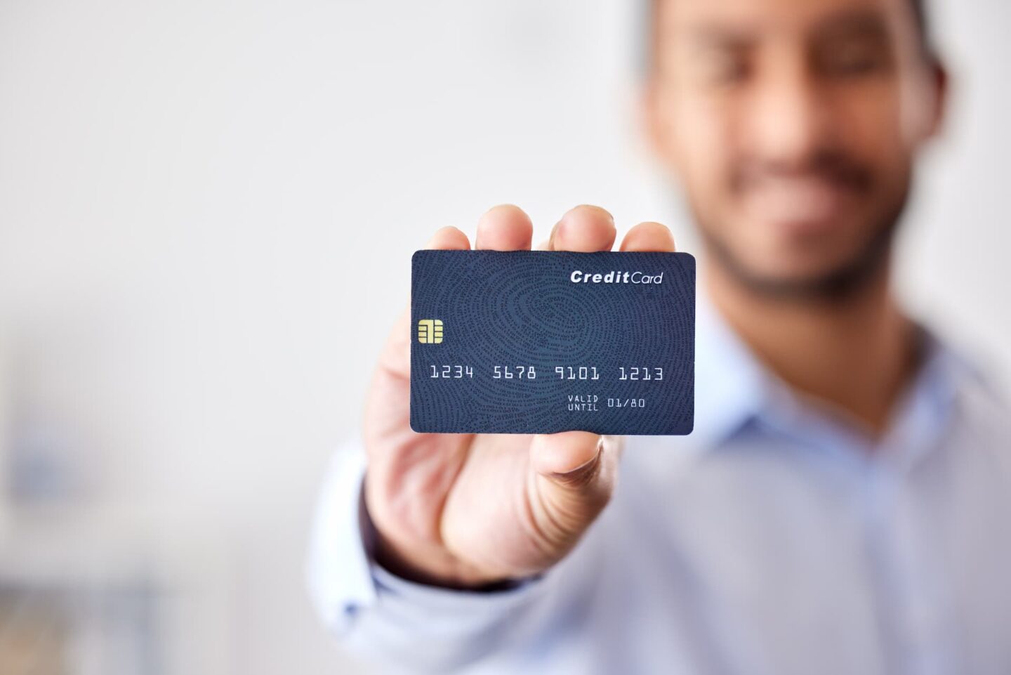 Blue credit card held by a smiling man in professional attire, emphasizing digital payments and financial services.