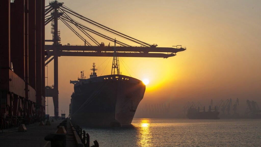 Large cargo ship docked at port during sunset with cranes in the background, logistics, shipping industry.