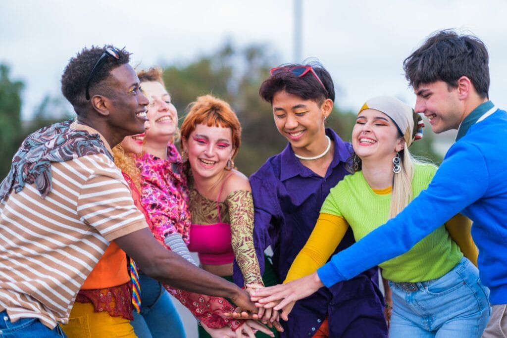 Diverse group of friends smiling and stacking hands together outdoors, celebrating unity and friendship.