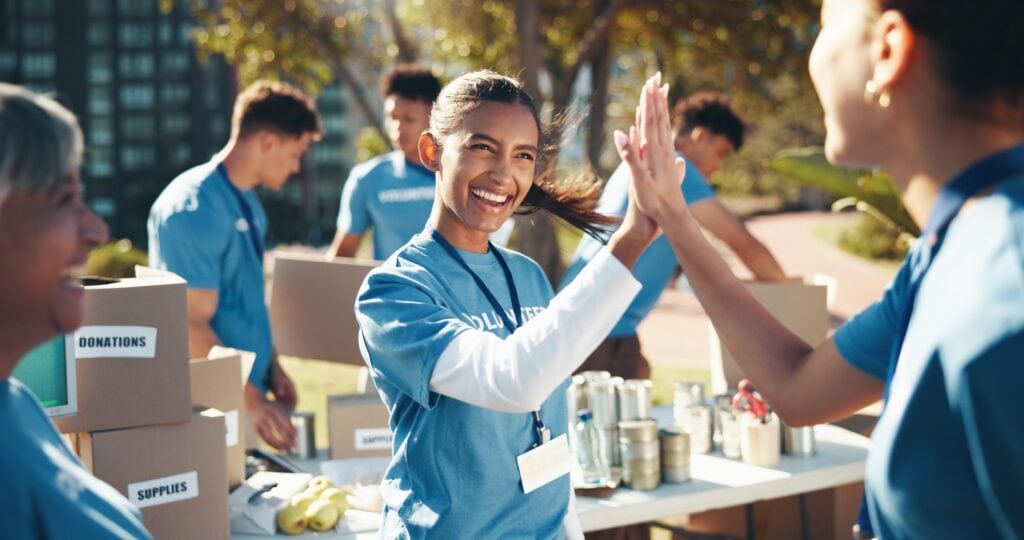 High-energy volunteers at charity event giving high five outdoors, supporting community causes.
