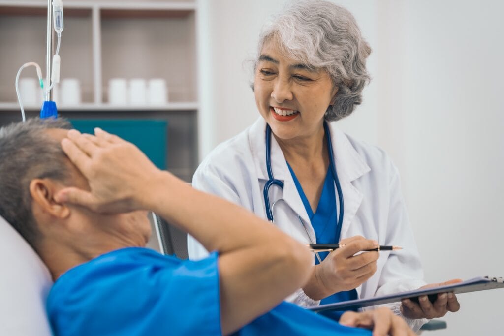 Comfortable hospital room with caring nurse assisting elderly patient during medical consultation.
