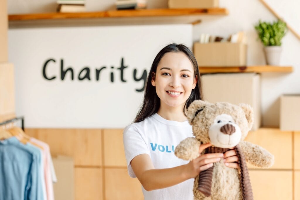 -volunteer woman donating teddy bear at charity event, smiling, community support, kindness.