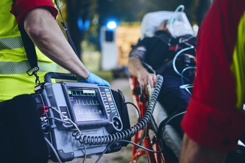 Emergency medical technician uses defibrillator on patient outdoors during rescue.