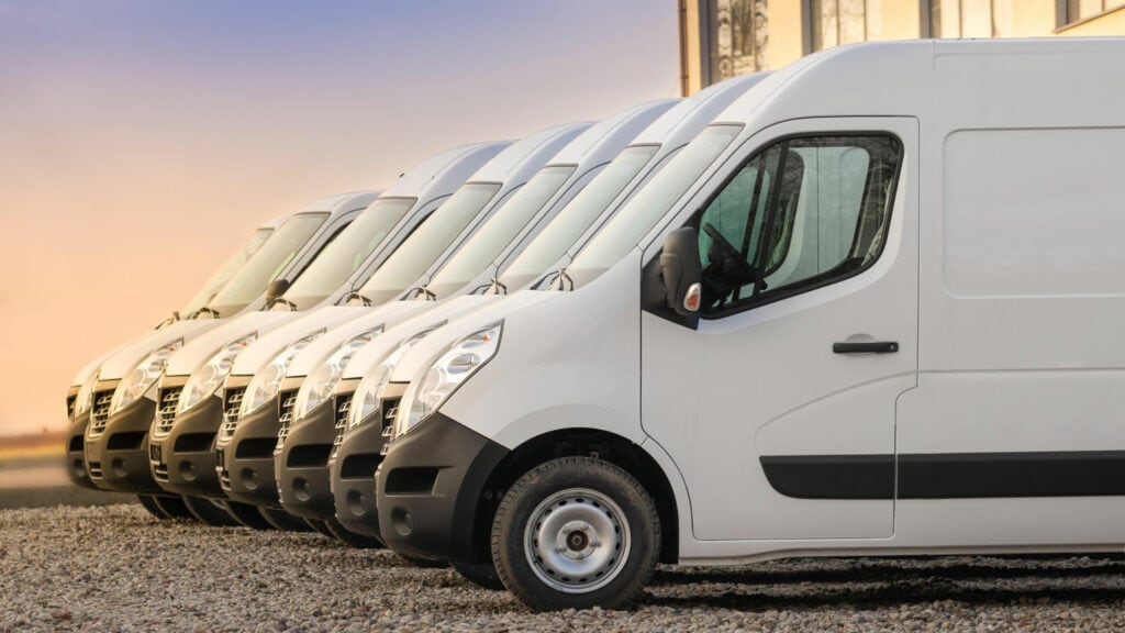 White commercial cargo vans parked in a row at sunset.