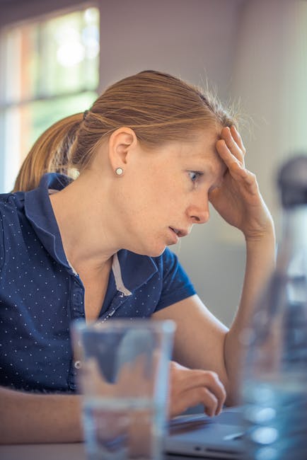 Overwhelmed woman working at desk, stressed from workload, experiencing frustration or fatigue.