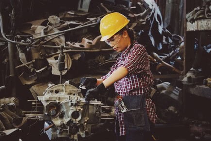 Young girl inspecting engine parts in a scrapyard for automotive recycling.
