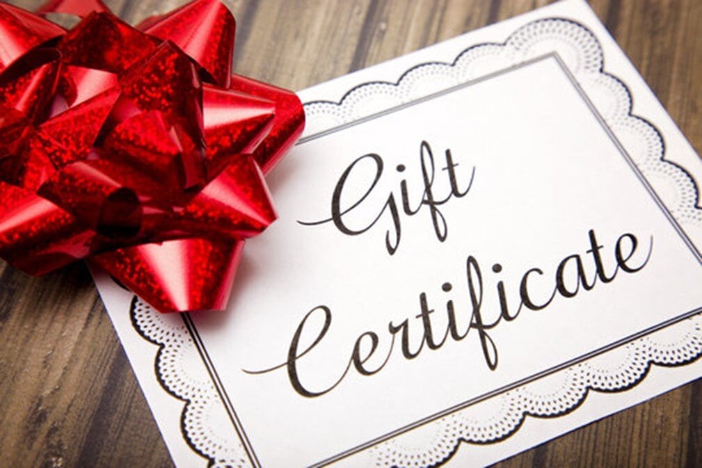 Bright red gift bow with a gift certificate on wooden surface.