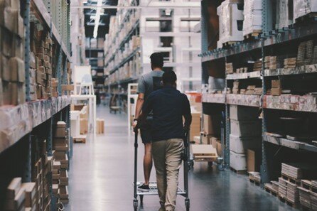 Efficient warehouse shopping with customers navigating aisle of storage and supplies.