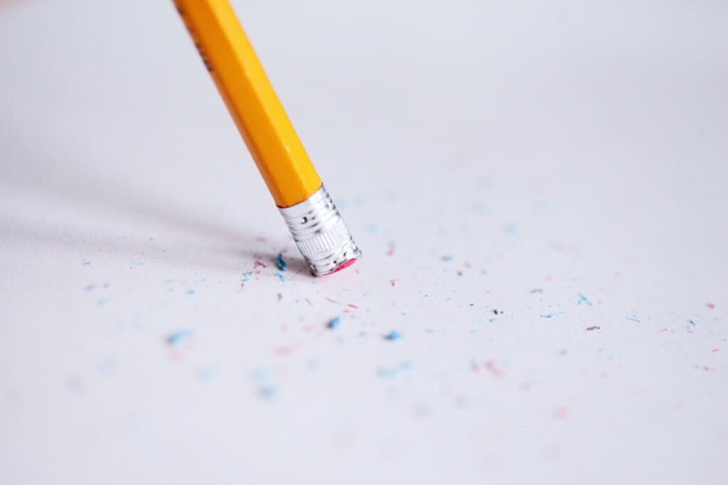 Bright yellow pencil erasing colorful scattered confetti on white paper, emphasizing stationery and creative tools.