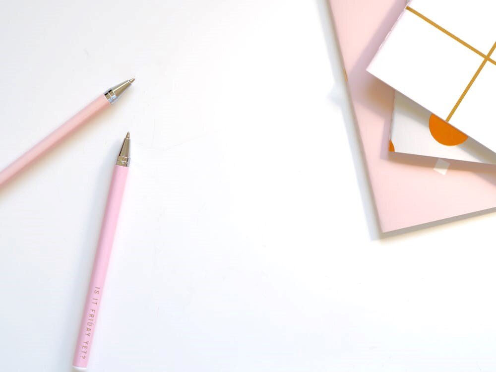 Pink pens and stationery on a white background with notebooks, emphasizing office supplies and organization.