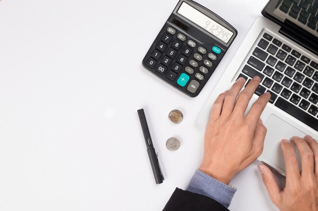 Calculator on a white desk with a laptop, pen, and coins, representing finance and accounting concepts.