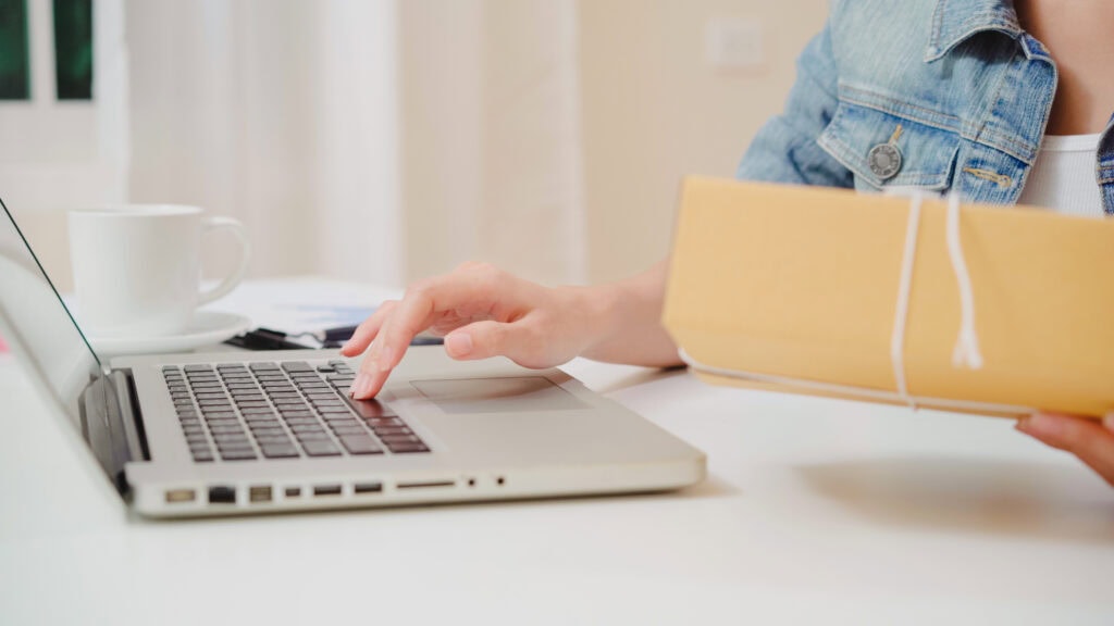 Person working with laptop and holding yellow folder in a modern workspace.