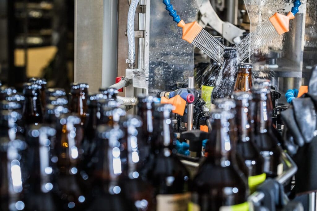 Industrial beverage bottle washing process with spray nozzles and water jets.