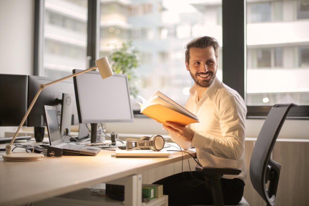 1. Man working at modern office desk with multiple monitors and files.