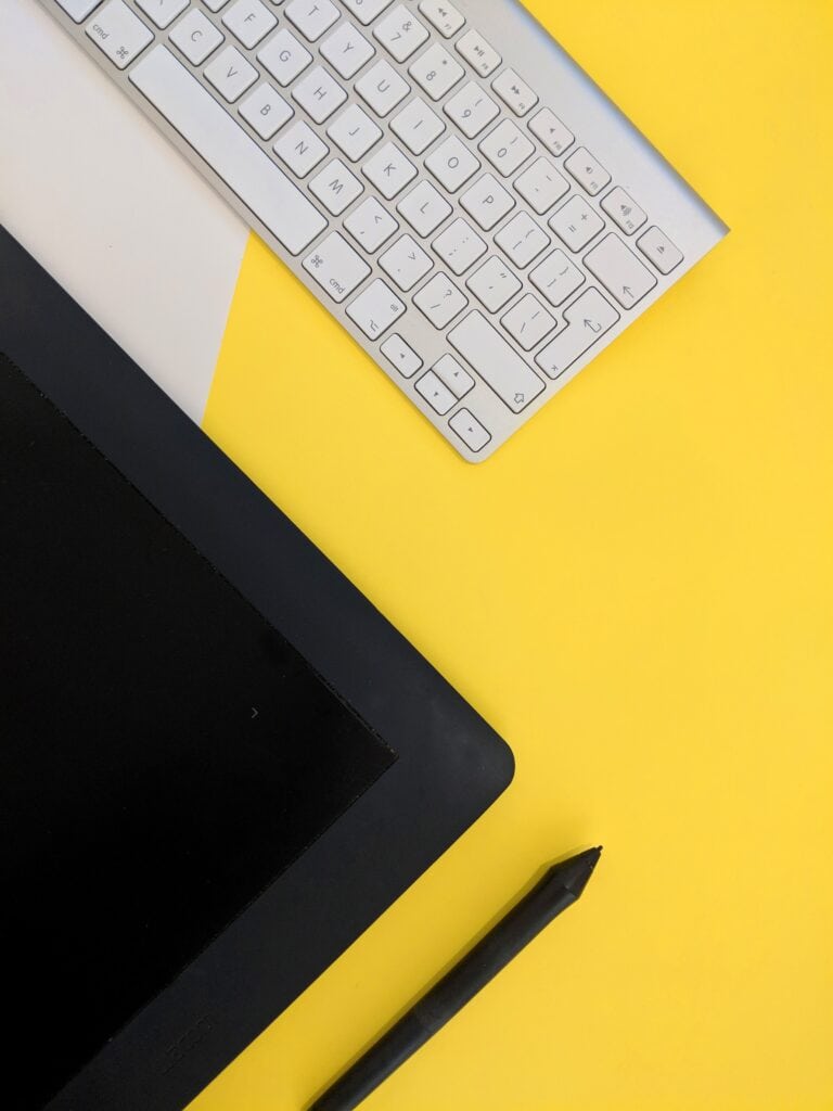 Bright yellow desk with graphics tablet, wireless keyboard, and stylus, ideal for digital art and design.