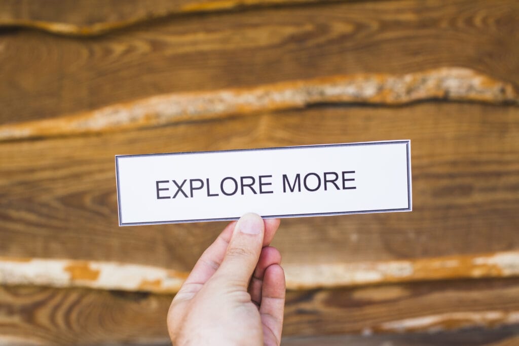 Explore more concept in business or technology with a hand holding a sign that says "Explore More" against a wooden background.