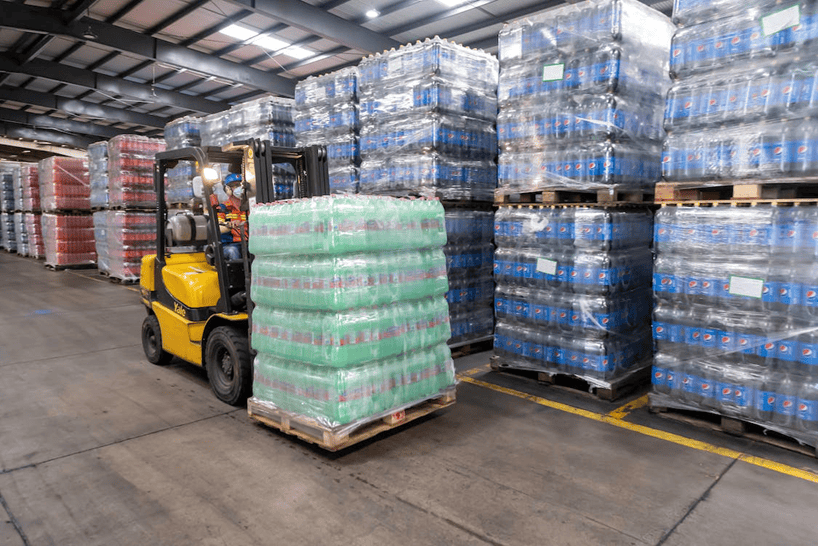 Stacked bottled beverages in a warehouse with forklift handling pallets for distribution.