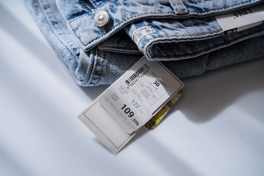 Denim jeans with price tags on white background, fashion retail, clothing store, apparel shopping.