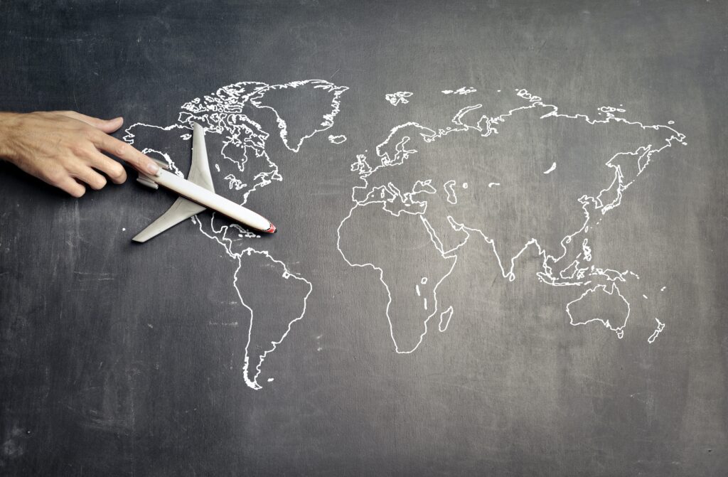Hand drawing a world map with white chalk on a blackboard, representing global business and travel.