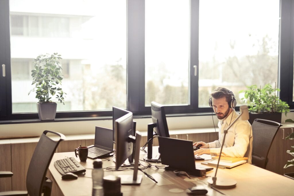 Focused man working at desk with multiple computer monitors in a modern office.