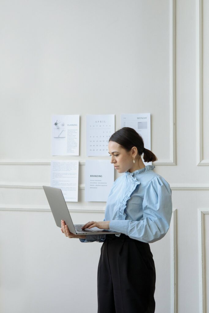 A woman working on a laptop in an office setting with planning and branding documents on the wall.