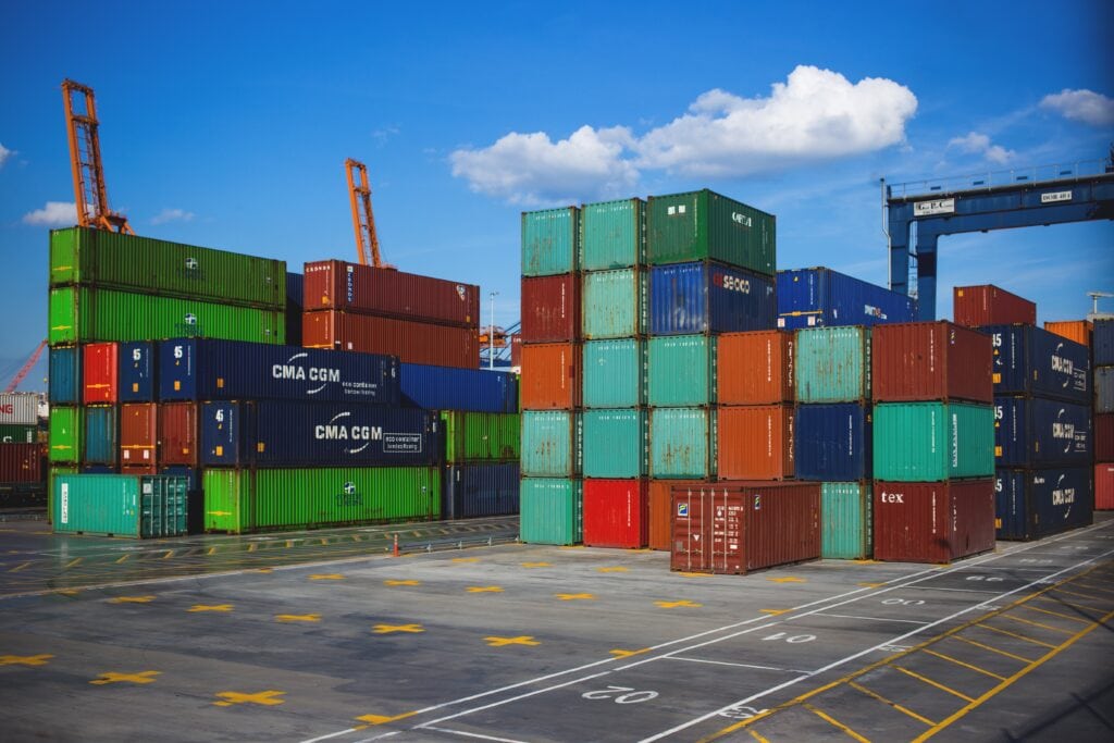 Colorful shipping containers stacked at a busy port against a bright blue sky.