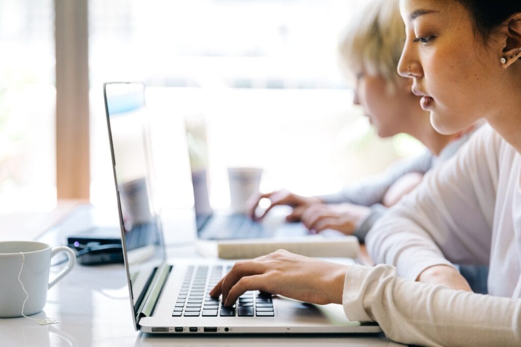 Modern women working on silver laptops in a bright, contemporary office setting with natural light.