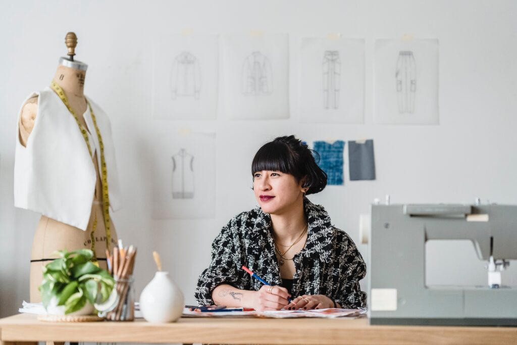 Stylish fashion designer working on clothing sketches in a creative studio with sewing patterns and dress forms.