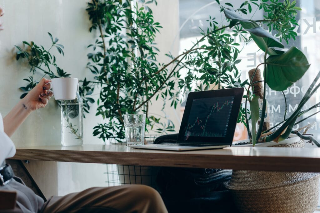 Bright workspace with laptop displaying stock chart, surrounded by lush green plants, promoting productivity and focus.