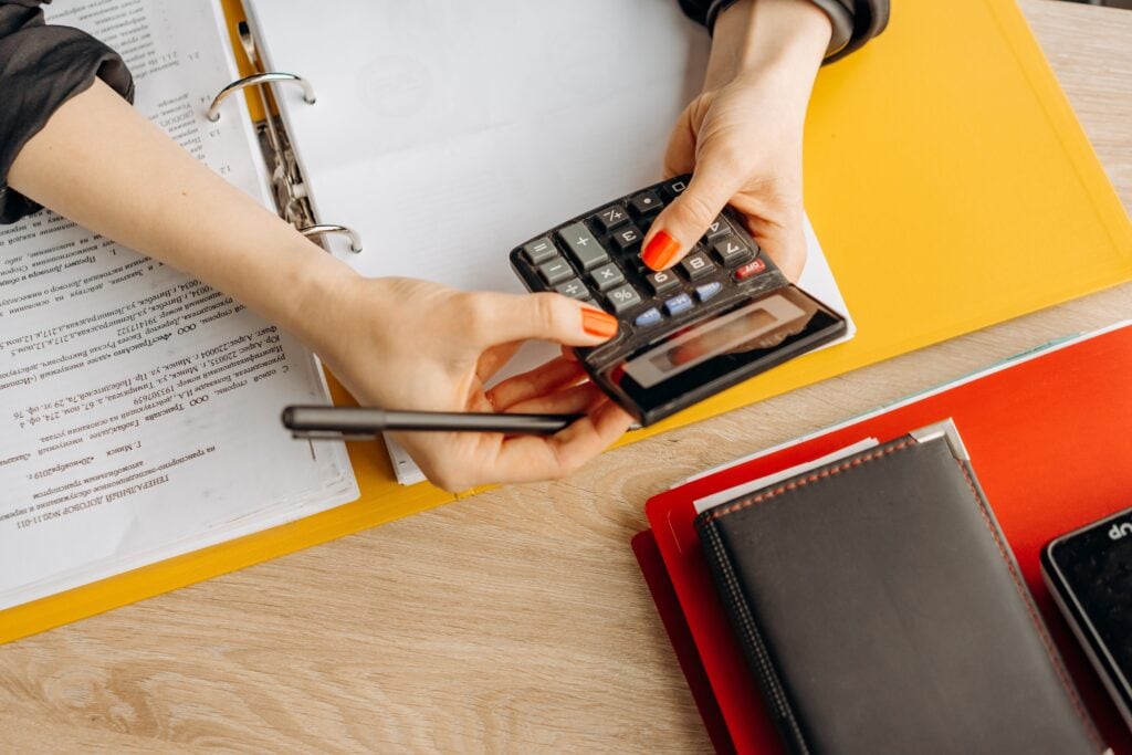 2. A person using a calculator with financial documents on a wooden desk.