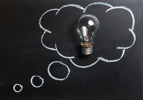 Light bulb in chalk-drawn thought bubble on chalkboard, symbolizing ideas and innovation.