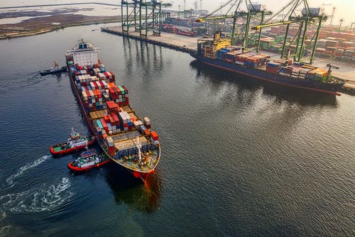 Cargo ship transporting containers at port with cranes in background during sunset.