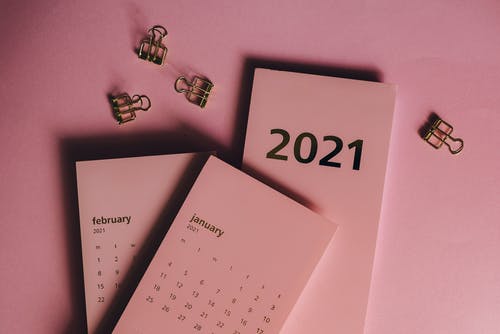 2021 desk calendar with February and January pages, pink background, and gold binder clips.