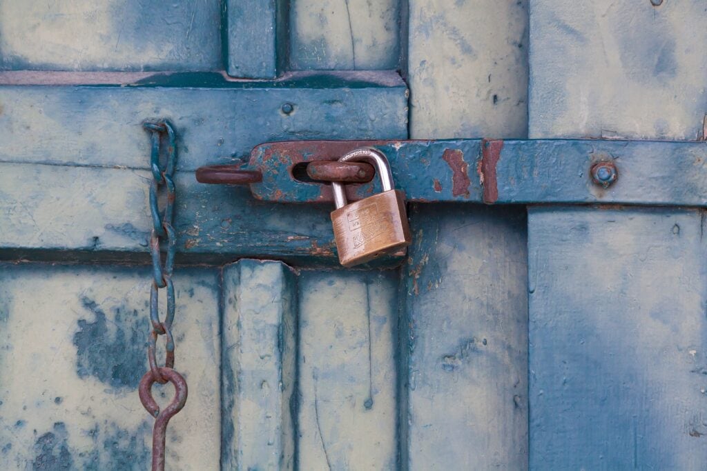 Lock and chain securing a weathered, blue wooden door with rust details.
