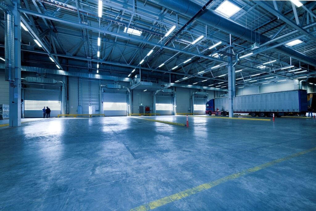 Bright industrial warehouse with large trucks, high ceilings, and modern LED lighting for logistics.