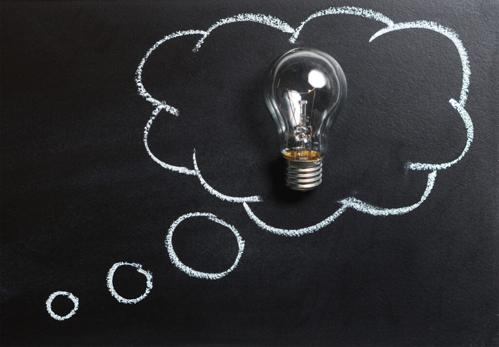 Innovative light bulb with chalk-drawn thought cloud on blackboard for creative ideas.