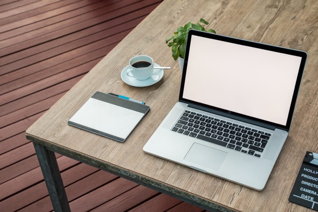 Clean workspace with laptop, tablet, coffee, and plant outdoors for remote work or productivity.