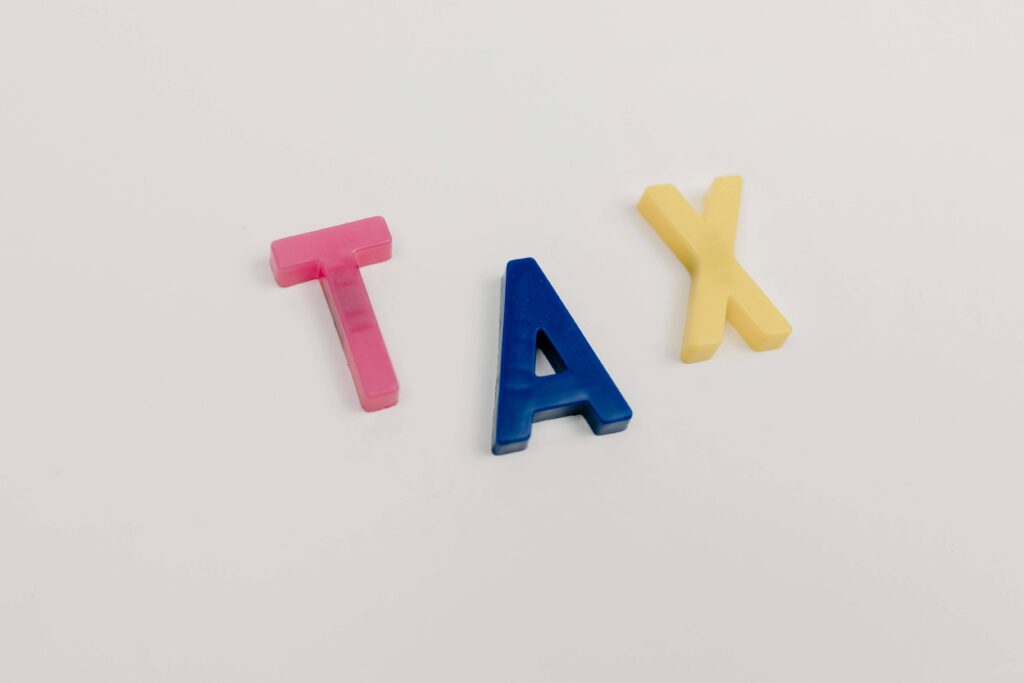 Colorful plastic letters spelling "TAX" on a white background.