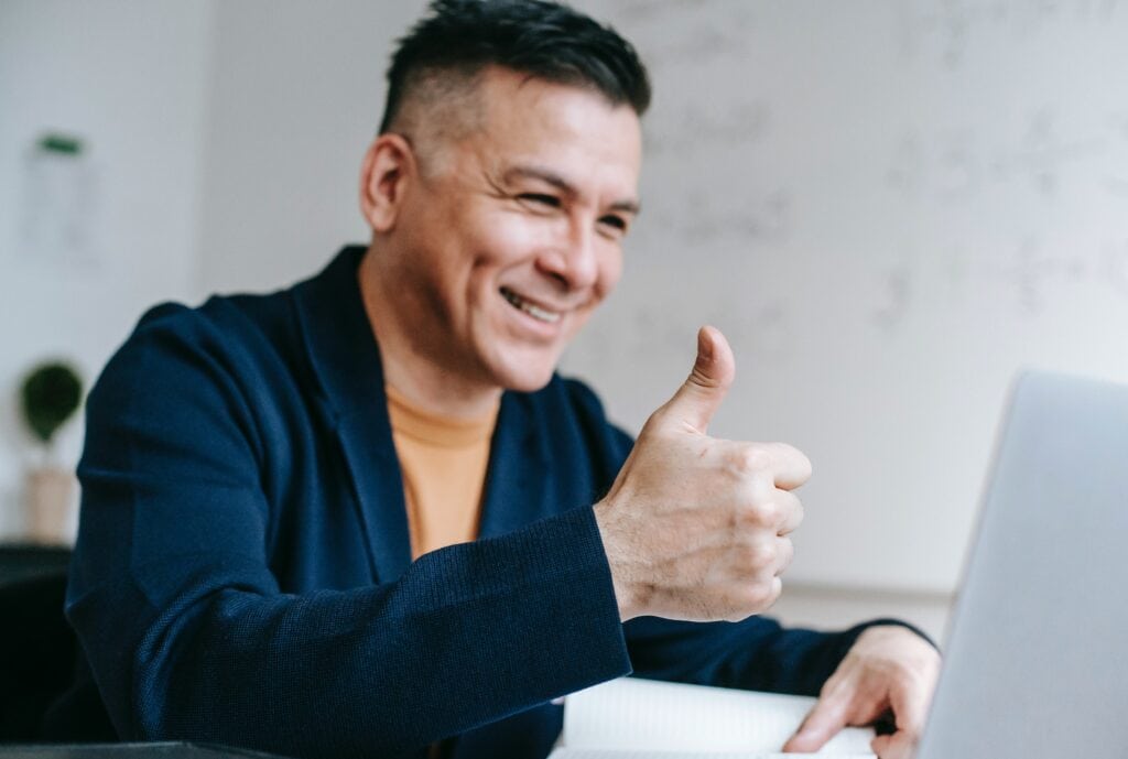 Smiling man giving thumbs-up in front of laptop, positive business success concept.