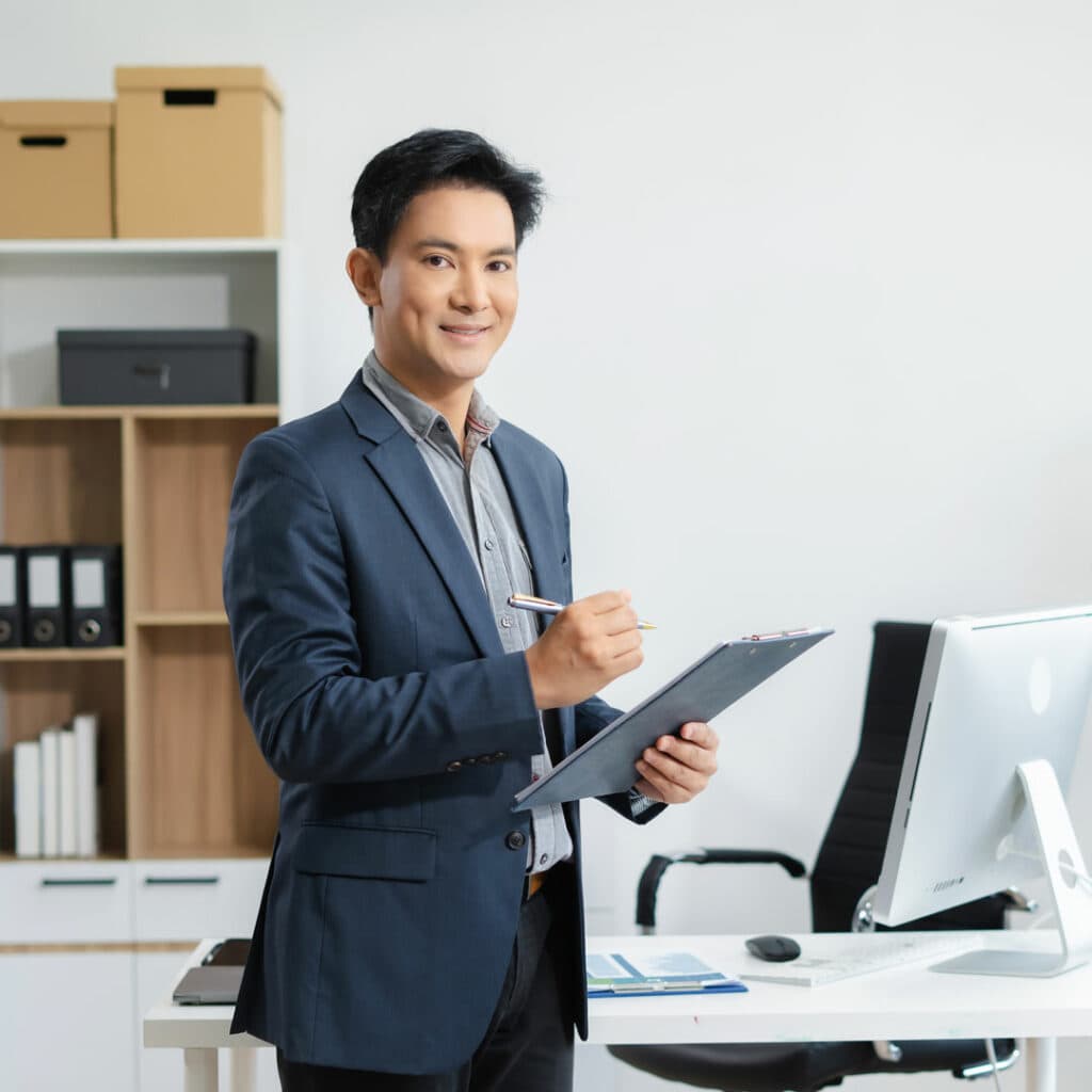 Professional businessman in office with clipboard and computer, representing business consulting and corporate services.