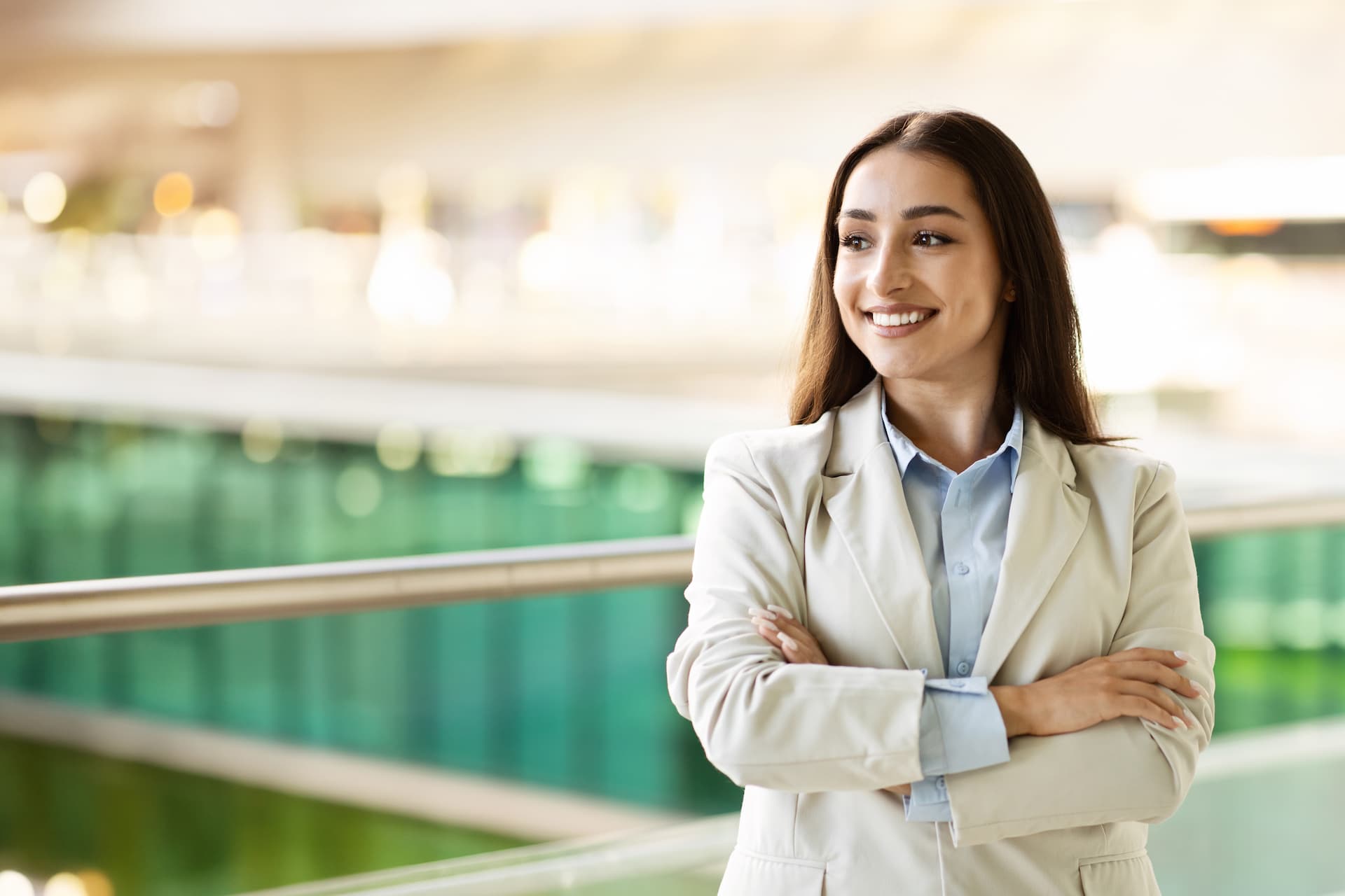 Multicultural businesswoman smiling, modern office environment, confident professional, corporate attire, cross arms.