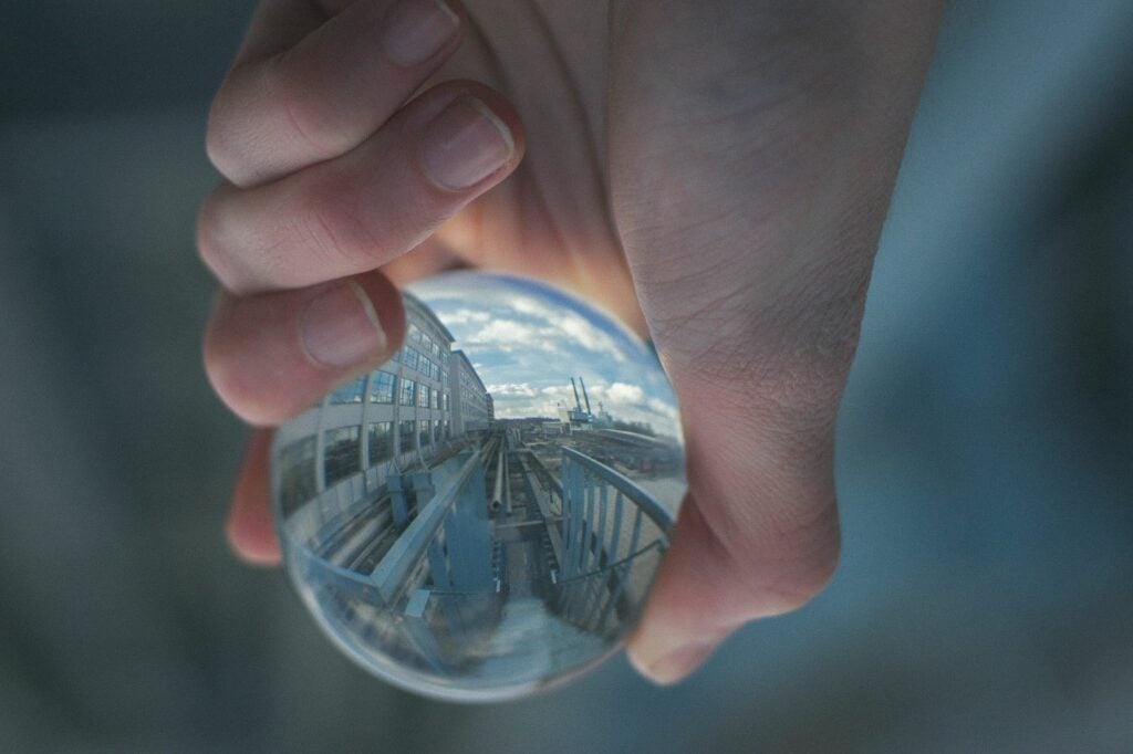 A crystal ball held in hand reflecting an industrial cityscape with buildings and cranes.