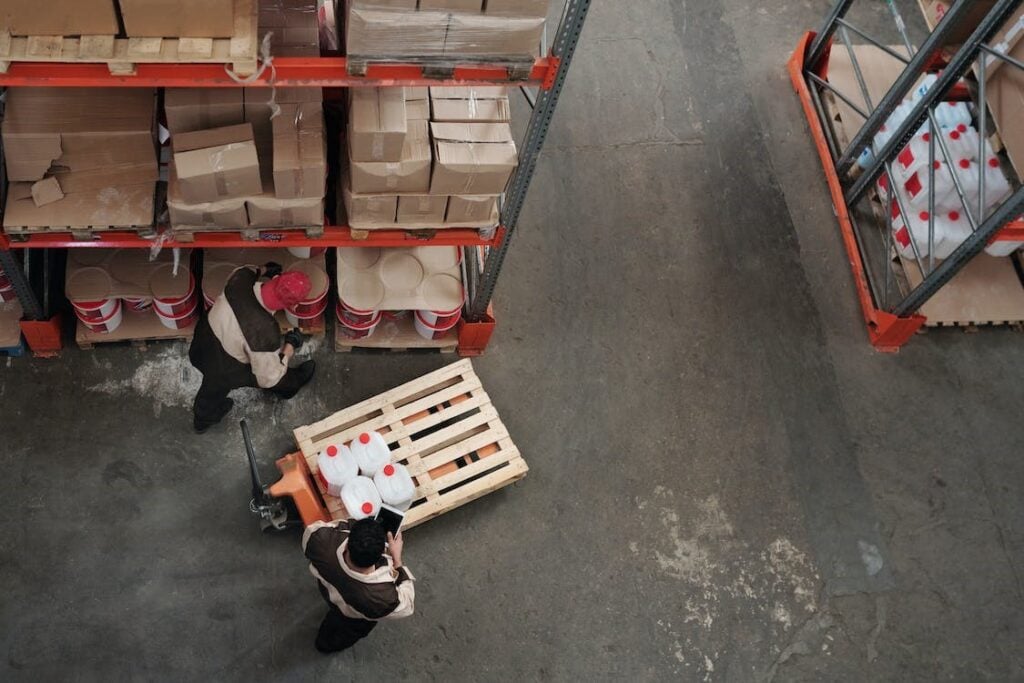 Stacks of cardboard boxes and plastic containers stored on metal shelving in a warehouse.