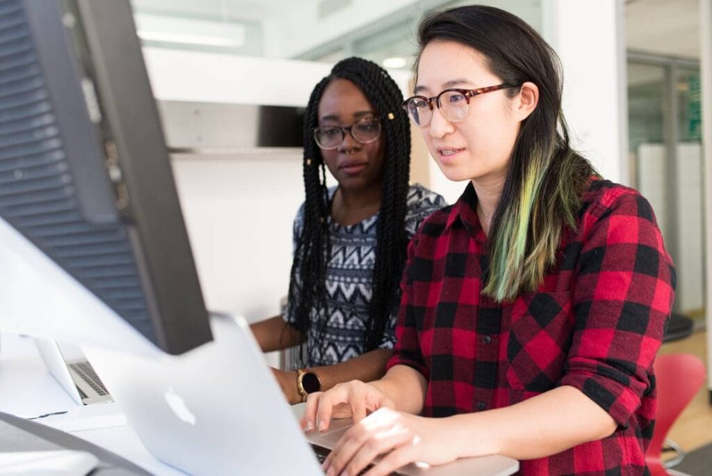 Diverse women working on laptops in an office setting, focusing on technology and collaboration.
