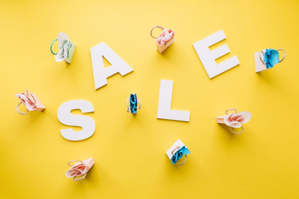 Colorful paper flowers with white "SALE" letters on a yellow background, promoting promotional offers.